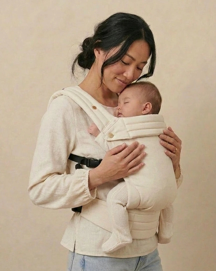 Maman portant bébé contre elle dans le porte‑bébé physiologique beige — parent et bébé endormis, portage poitrine confortable