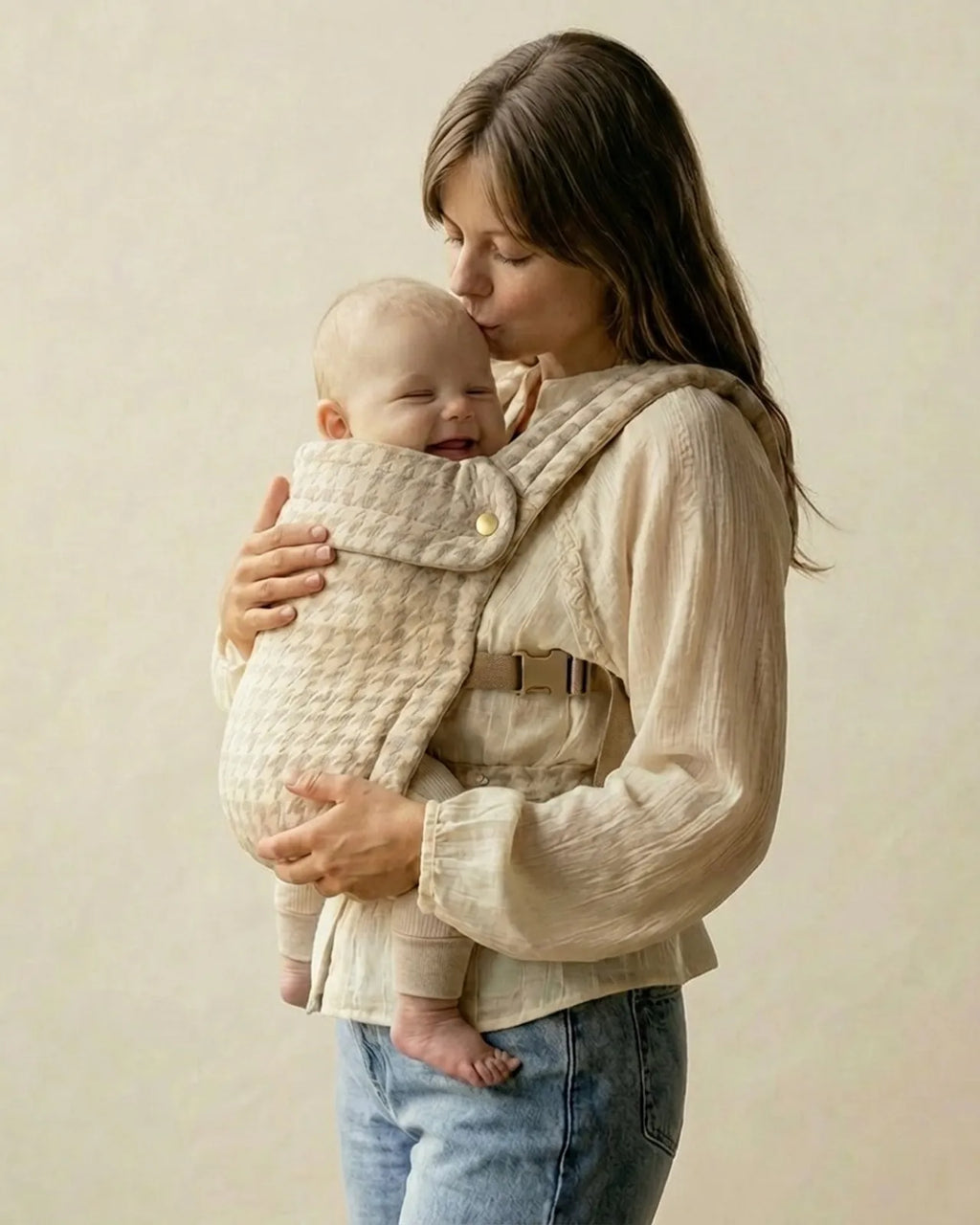 Femme embrassant bébé porté dans le porte-bébé physiologique gris chiné à motif dent-de-poule — moment tendre, confort et maintien ergonomique