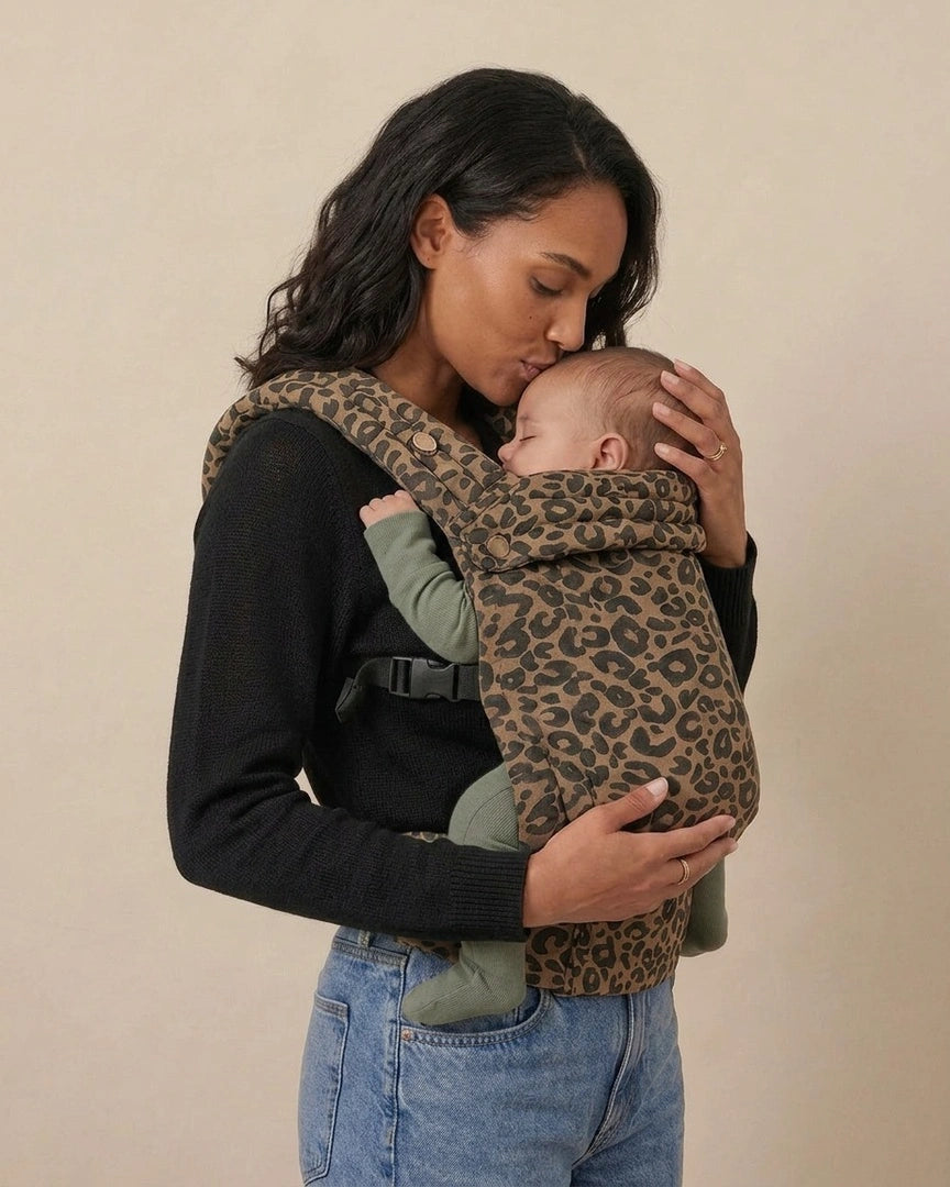 Parent embrassant bébé porté dans le porte‑bébé physiologique marron motif léopard — moment tendre, confort et maintien ergonomique