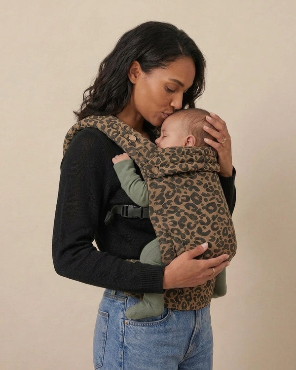Parent embrassant bébé porté dans le porte‑bébé physiologique marron motif léopard — moment tendre, confort et maintien ergonomique