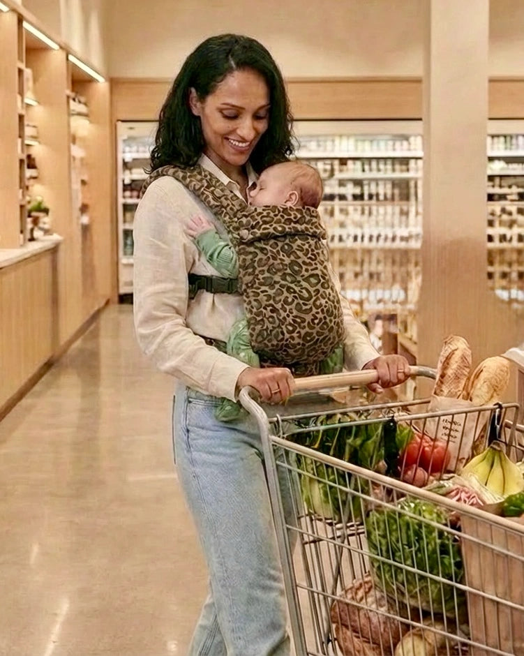 Parent portant bébé dans le porte‑bébé physiologique marron motif léopard au supermarché, près d’un caddie — portage pratique pour les courses
