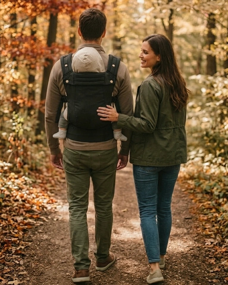 Parent portant bébé dans le porte‑bébé physiologique noir en forêt — promenade en nature, confort et maintien ergonomique